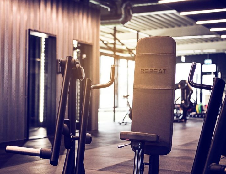 Moderne styrketræningsmaskiner i kommercielt fitnesscenter med REPEAT-logo på ryglæn